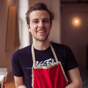 young man smiling into camera wearing a red apron