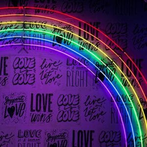 Rainbow coloured neon lights illuminating a background that reads "love" repeatedly