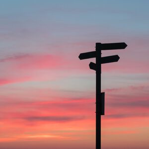 Directional sign silhouette against a sunset background