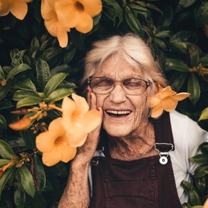 An older woman smiling amongst bright orange flowers